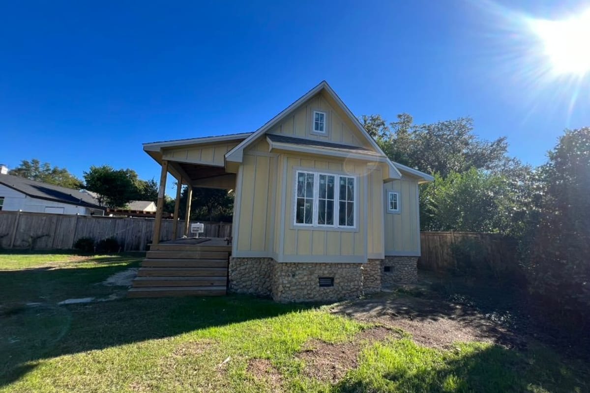Pale yellow cottage with white trim and a new covered porch in bright sun