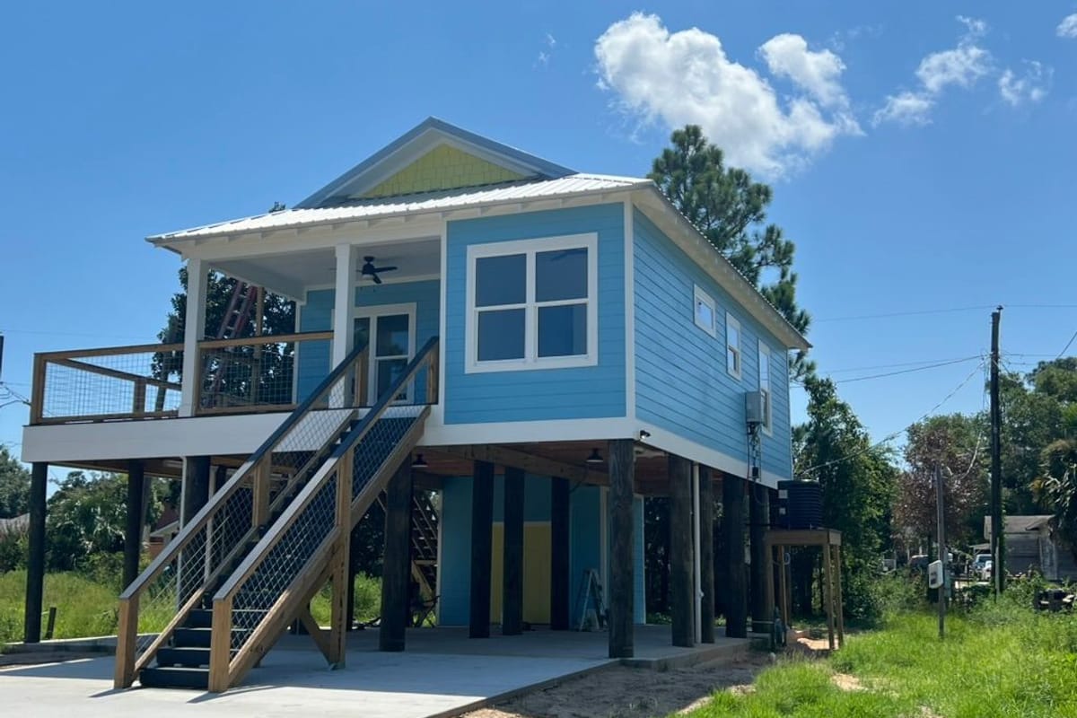 Raised blue coastal house with white trim and a new deck staircase