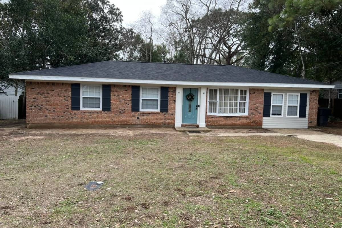 Brick ranch house with newly painted black shutters, white trim and a teal front door