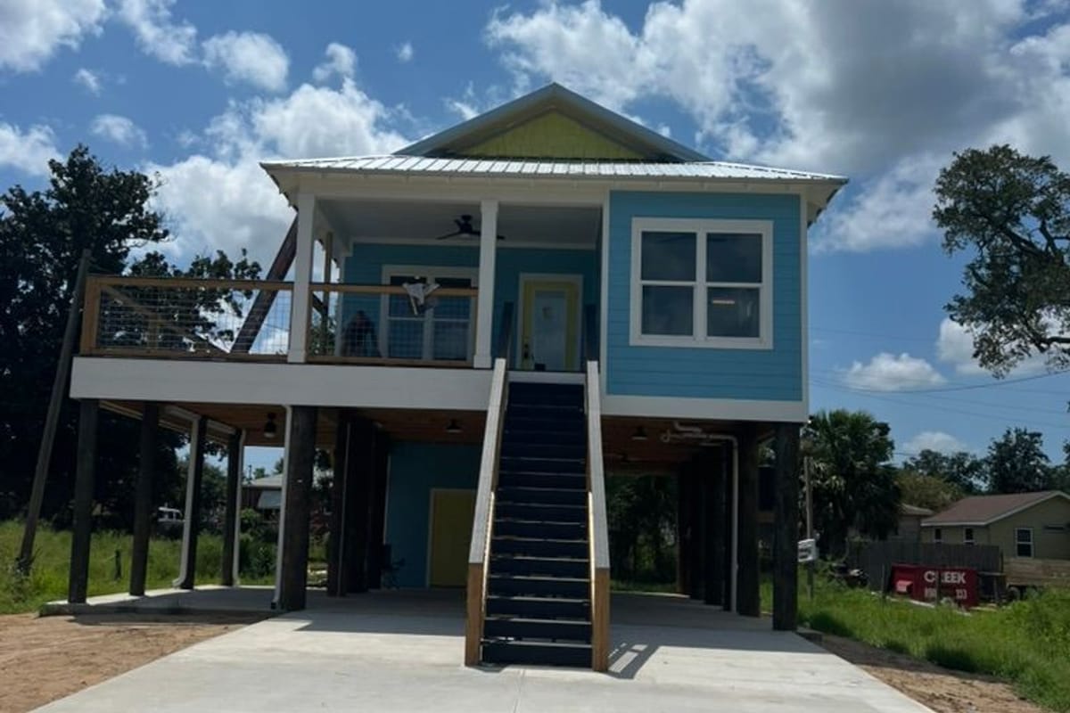 Raised blue house with white trim over a new concrete driveway