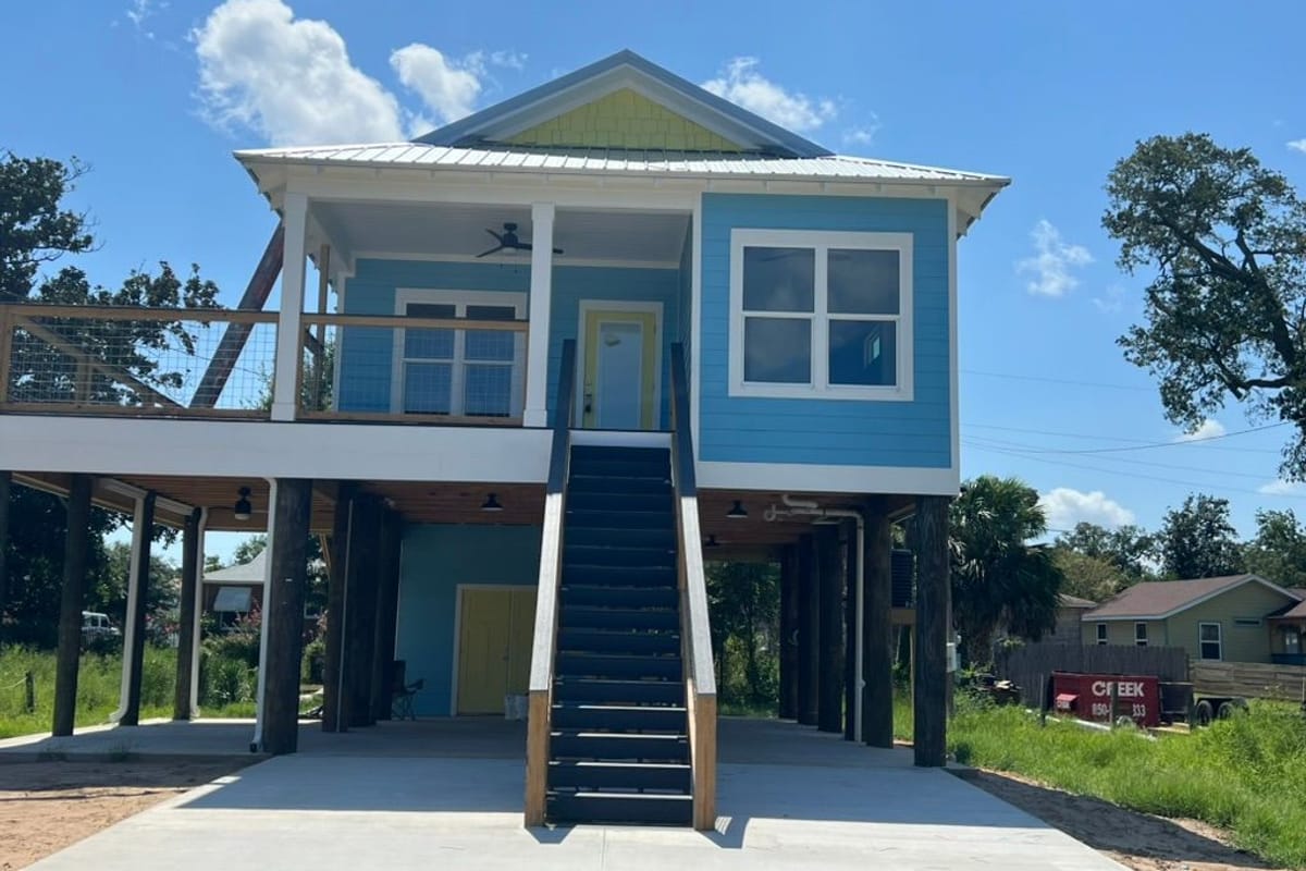 Raised blue coastal house with white trim and a dark staircase