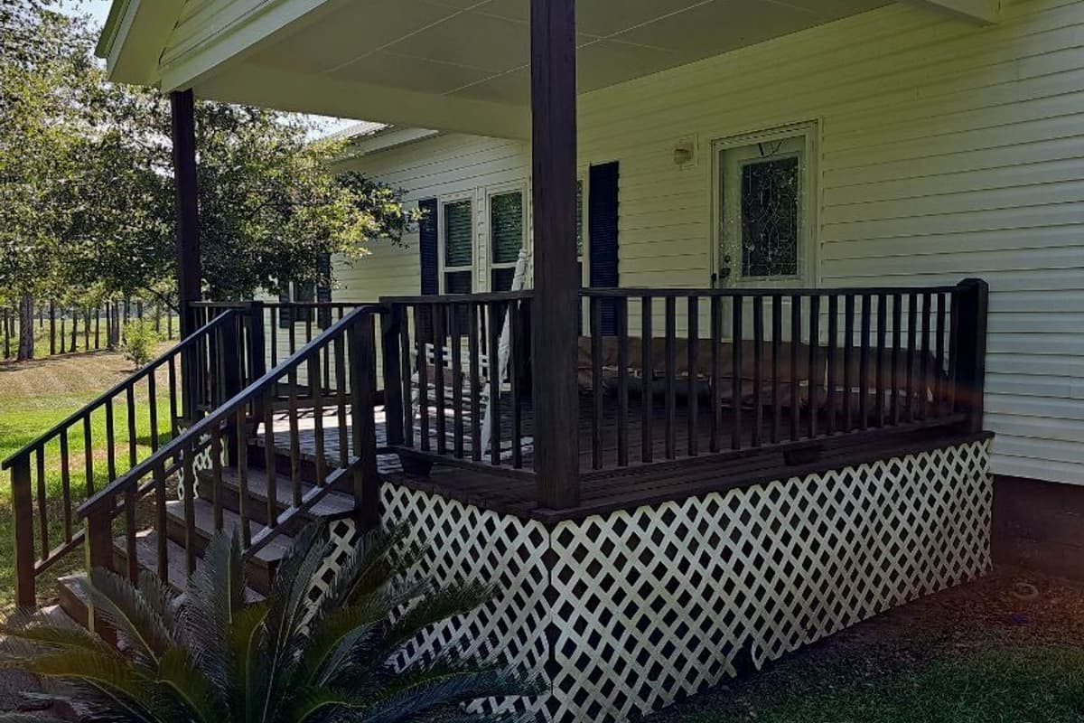 Covered porch with a dark-stained deck and railings on a yellow cottage