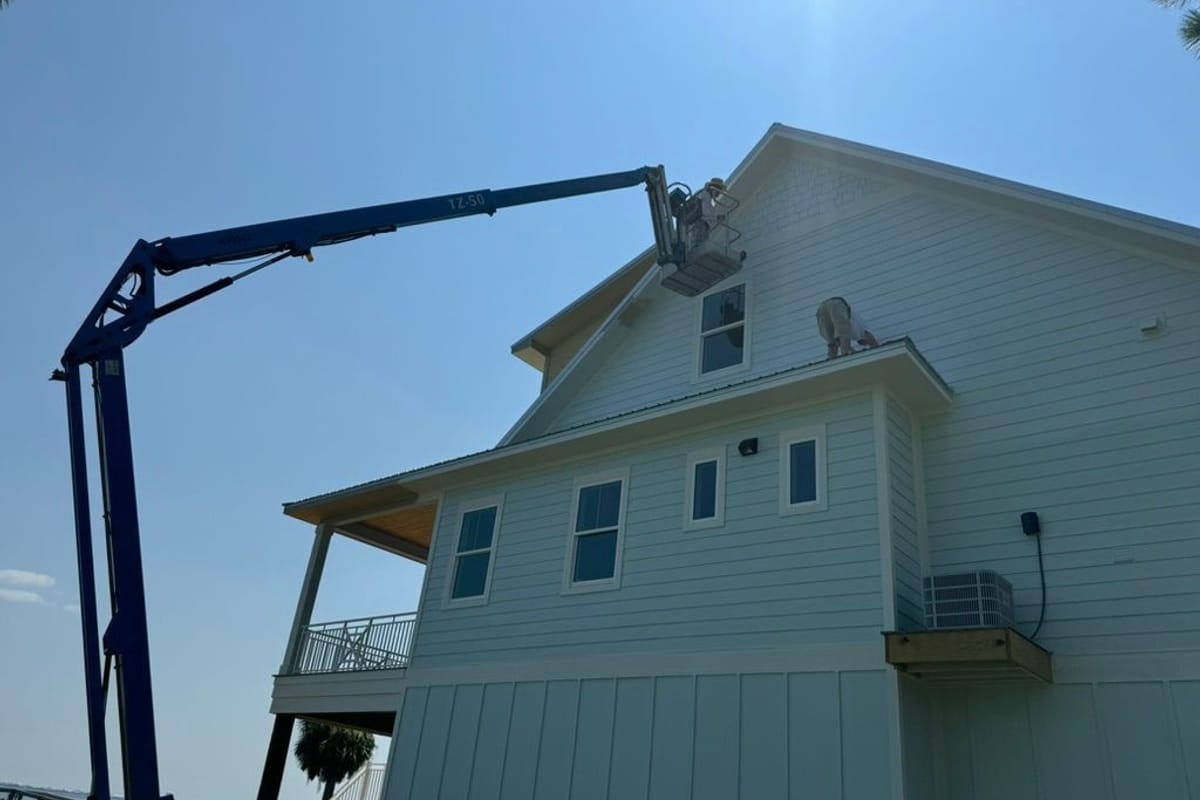 Boom lift reaching the second storey of a white house during exterior painting