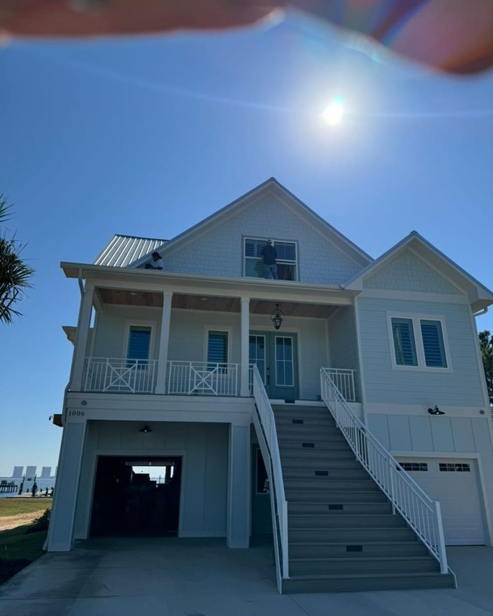 Two-storey raised coastal home with a freshly painted white exterior, black-framed windows and a white porch staircase