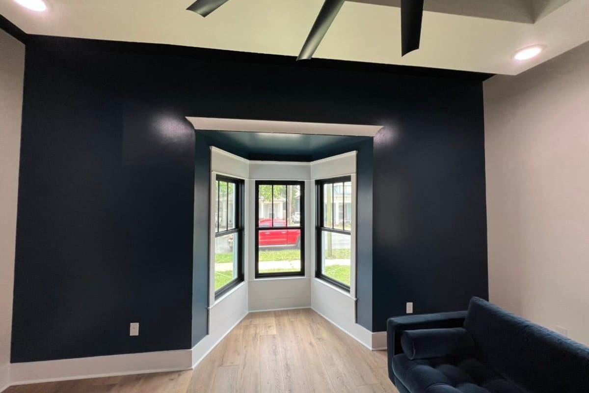 Living room with a charcoal accent wall around a bay window and dark ceiling beams